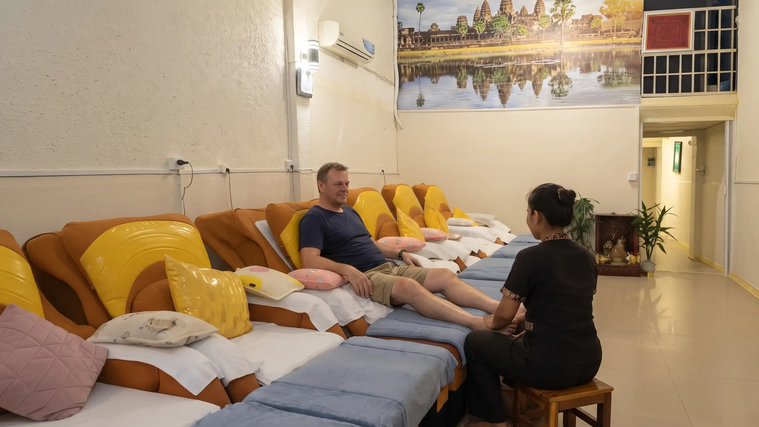A guest receiving a foot massage in one of the wide reclining chairs at Amiga, beneath the Angkor Wat mural